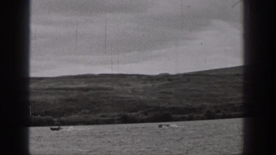 1938 Washington 8mm frame showing a small boat on rippled lake water below a low shoreline and overcast sky.