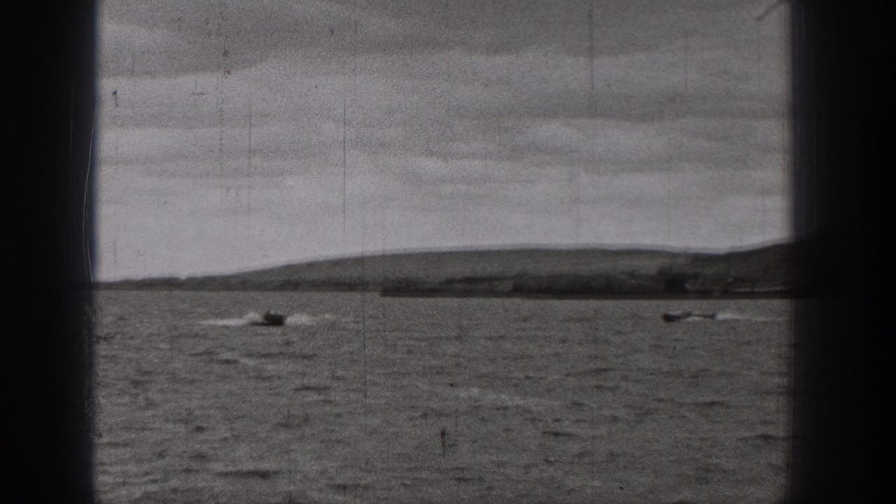 1938 Washington 8mm frame with two small boats on a calm lake, low shoreline, hills, and dark gate borders.