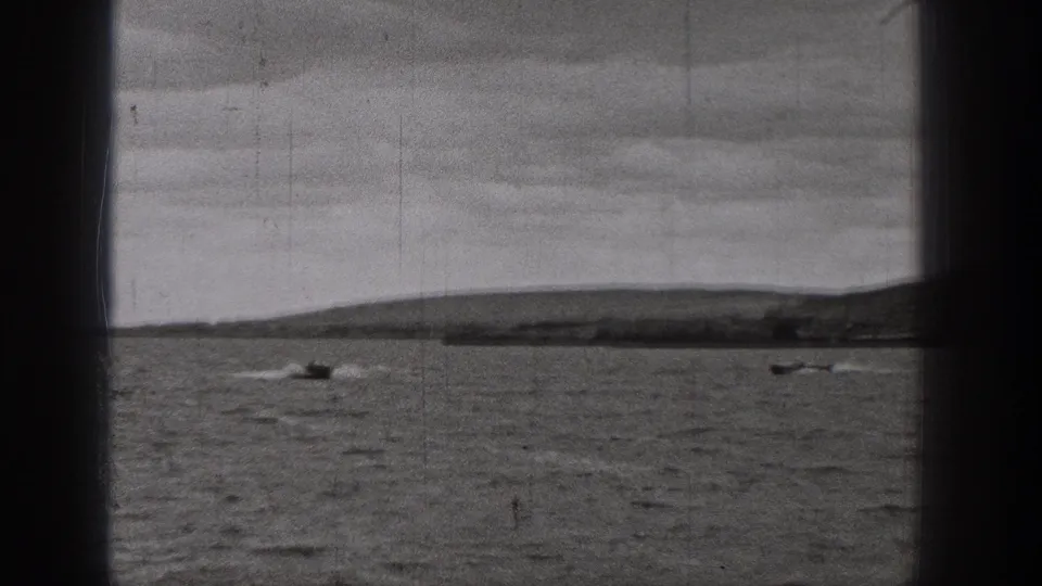 1938 Washington 8mm frame with two small boats on a calm lake, low shoreline, hills, and dark gate borders.