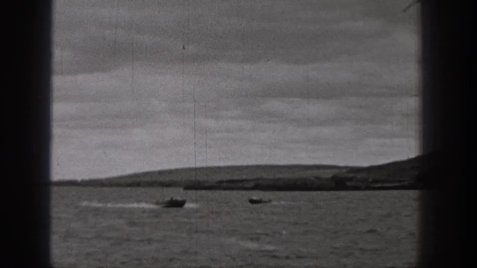 1938 Washington home-movie frame showing two boats on open lake water, with hills and an overcast sky in the distance.