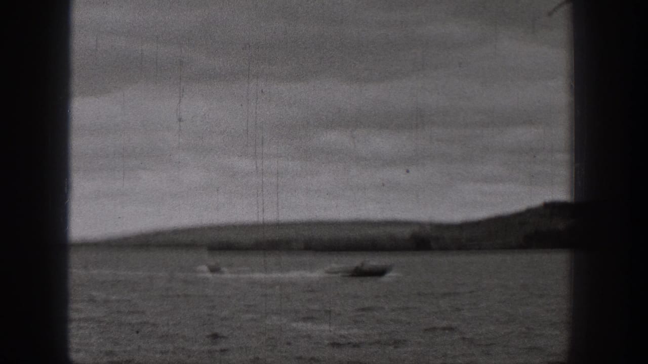 1938 Washington 8mm frame showing a small boat on a lake, distant landforms, overcast sky, and visible film gate edges.