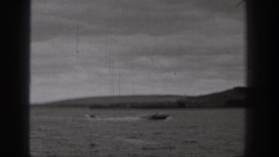 1938 Washington 8mm frame showing a small boat on a lake, distant landforms, overcast sky, and visible film gate edges.