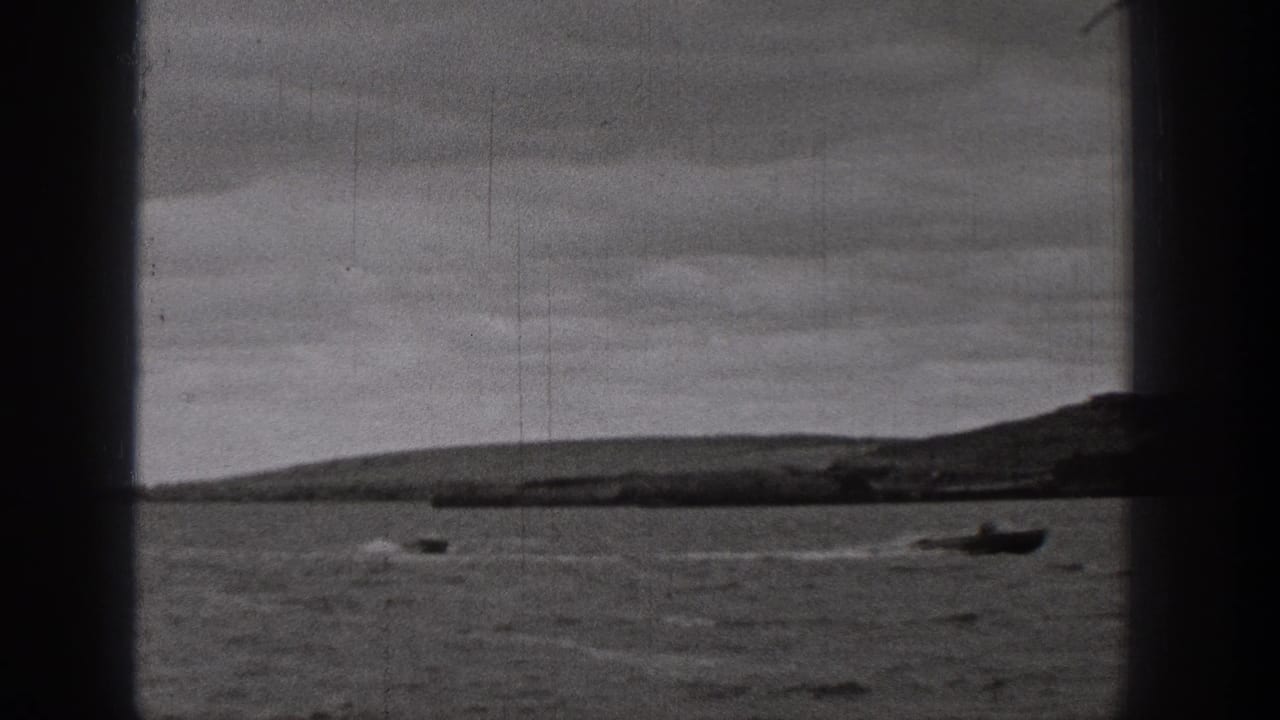1938 Washington home-movie frame showing a small motorboat leaving a wake across dark lake water with low hills in the distance.