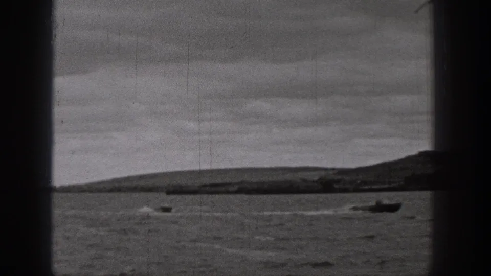 1938 Washington home-movie frame showing a small motorboat leaving a wake across dark lake water with low hills in the distance.