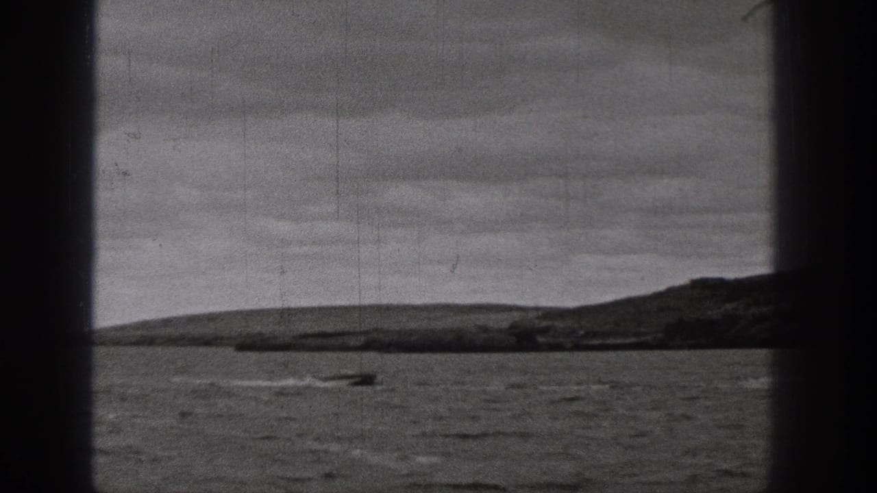 Black-and-white 8mm view of a motorboat crossing open water in Washington, with a low shoreline and dark gate edges visible.