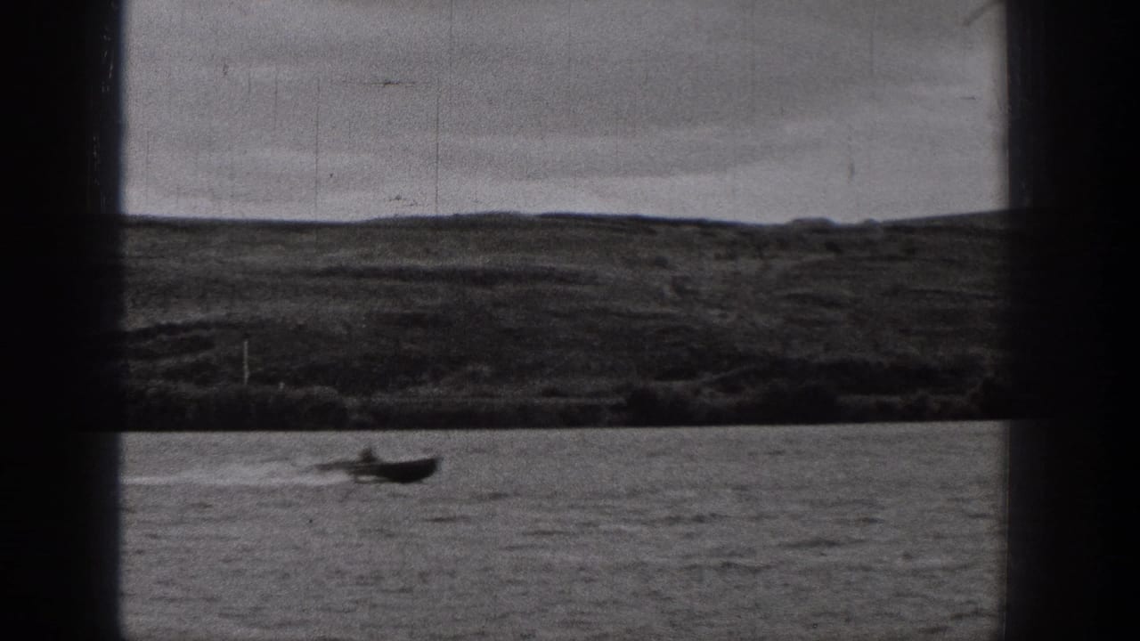 1938 Washington 8mm frame with a small boat near the lower edge of the water, backed by a broad dark hillside and overcast sky.