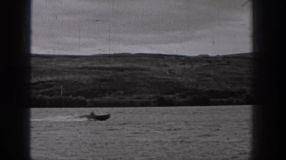 1938 Washington 8mm frame with a small boat near the lower edge of the water, backed by a broad dark hillside and overcast sky.