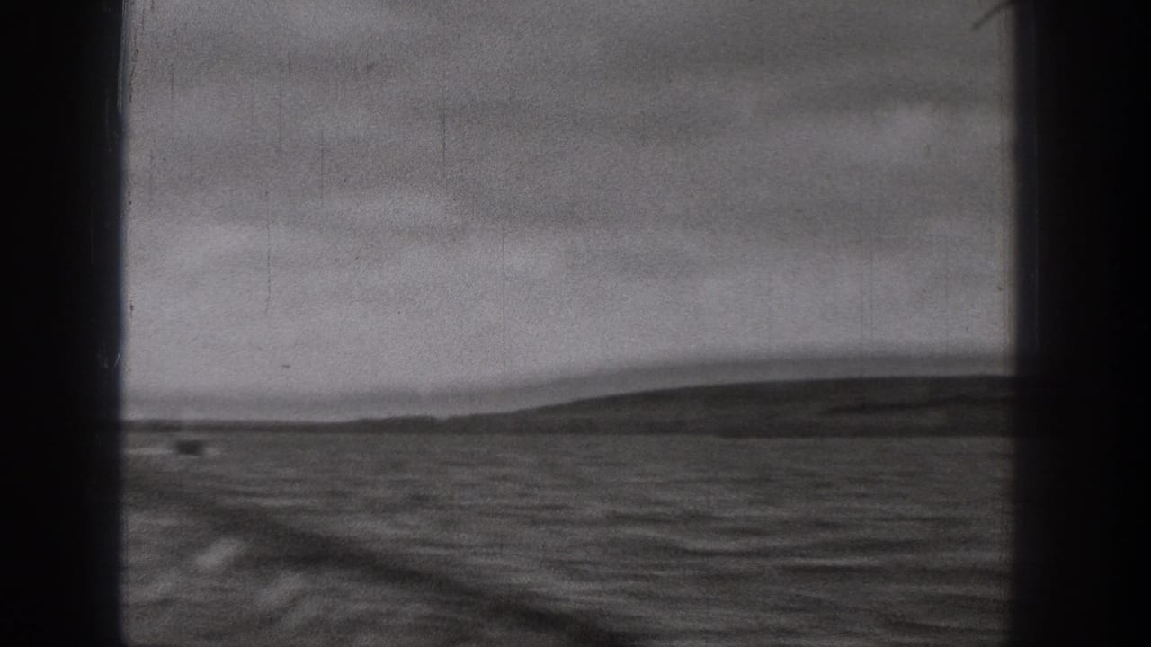 1938 Washington home-movie frame looking through a dark window frame toward rippled water and low hills in the distance.