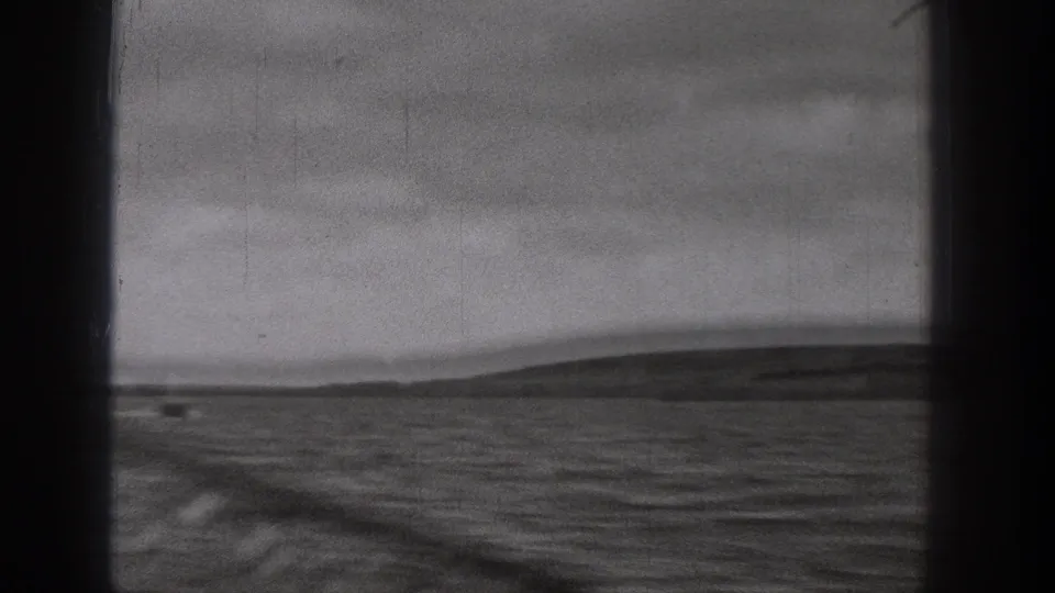 1938 Washington home-movie frame looking through a dark window frame toward rippled water and low hills in the distance.