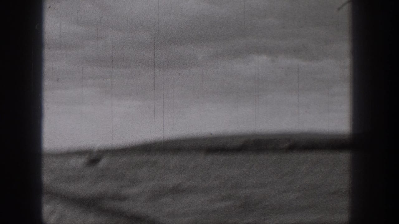 Window-framed view of rough water and a blurred shoreline under cloudy sky.