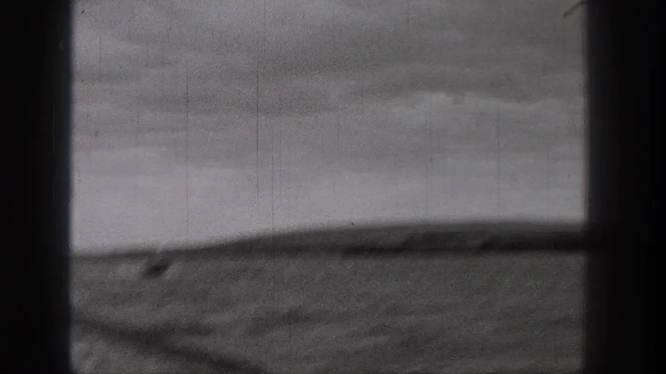 Black-and-white 8mm view from Washington, looking past a vertical window bar toward rough water and a soft distant shoreline.