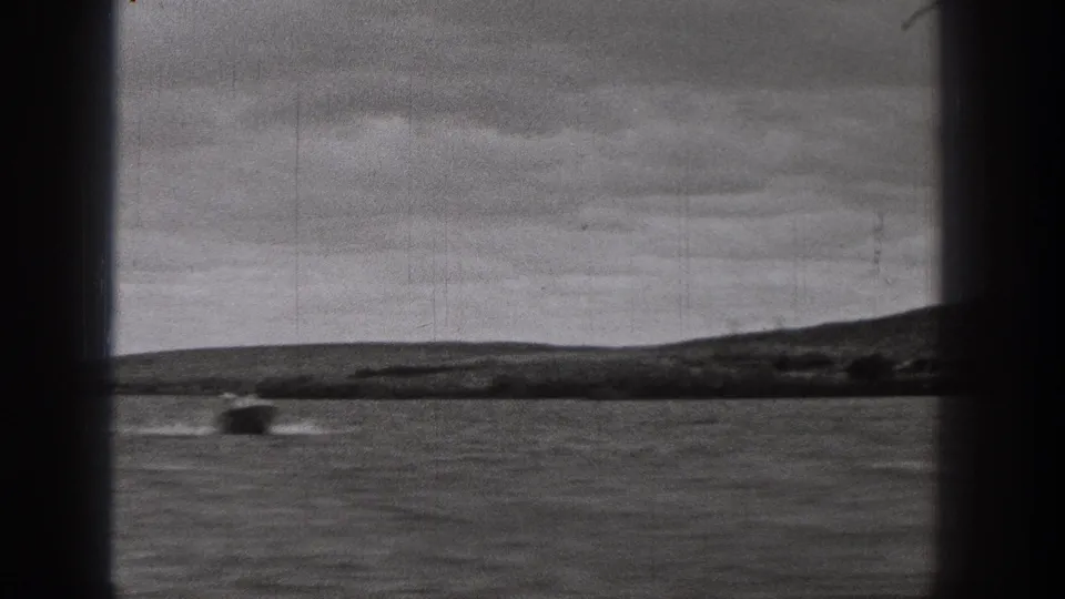 1938 Washington 8mm frame showing a small boat moving across rippled water beyond a dark window frame and distant shore.