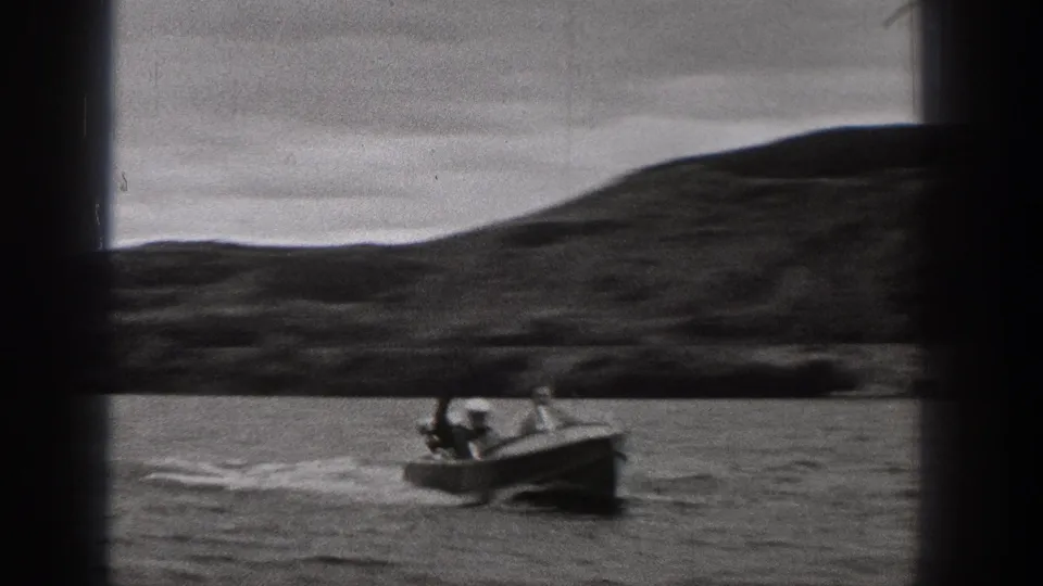1938 Washington 8mm frame showing a small motorboat moving across a mountain lake under a cloudy sky.