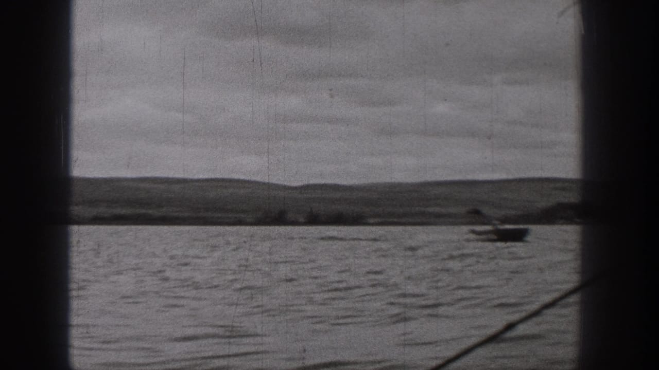 Wide 1938 Washington 8mm lake view with distant hills, cloudy sky, and a small boat near the right side.
