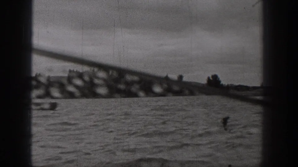1938 Washington home-movie frame showing choppy water, distant shoreline, and a small boat partly obscured by window framing.