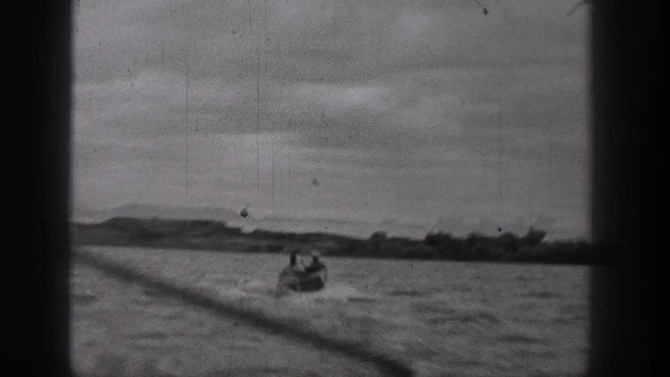 Distant small motorboat on a Washington waterway in 1938, filmed through a window with soft focus and scratches.