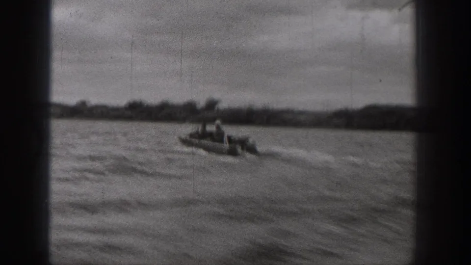 1938 Washington frame showing a small open motorboat with visible occupants moving across choppy water near a tree-lined shore.