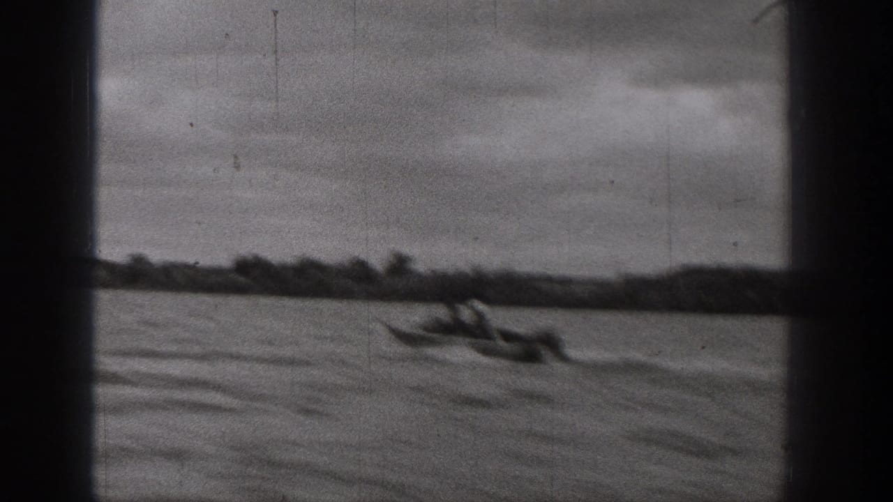 1938 Washington home-movie frame showing a small motorboat crossing a lake with a distant shoreline and cloudy sky.