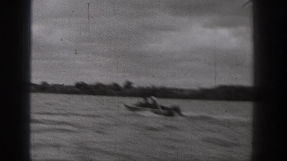 1938 Washington home-movie frame showing a small motorboat crossing a lake with a distant shoreline and cloudy sky.