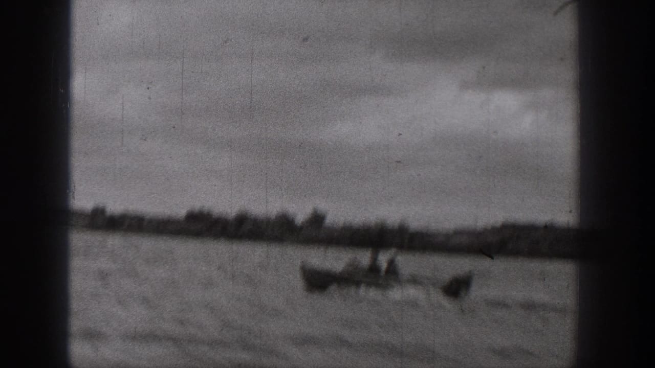 1938 Washington frame with a motorboat on a lake, viewed through dark frame-edge obstructions with clouds above the shoreline.