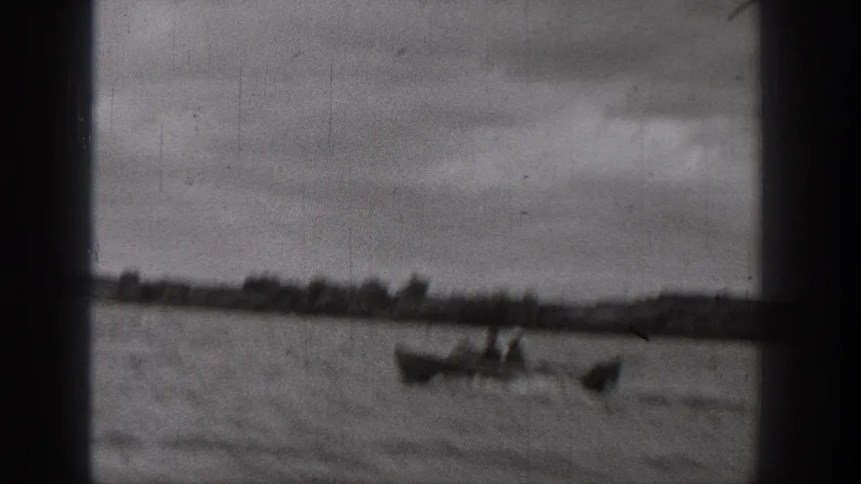 1938 Washington frame with a motorboat on a lake, viewed through dark frame-edge obstructions with clouds above the shoreline.