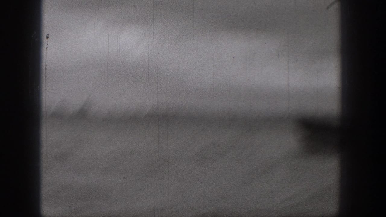 1938 Washington 8mm frame showing blurred water, a distant tree-lined shore, and dark film or boat edges during fast movement.