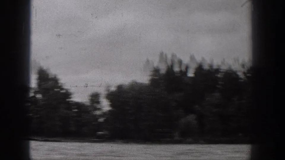 1938 Washington lake view from a moving boat, with open water, dark edge obstruction, and blurred trees along the far shore.