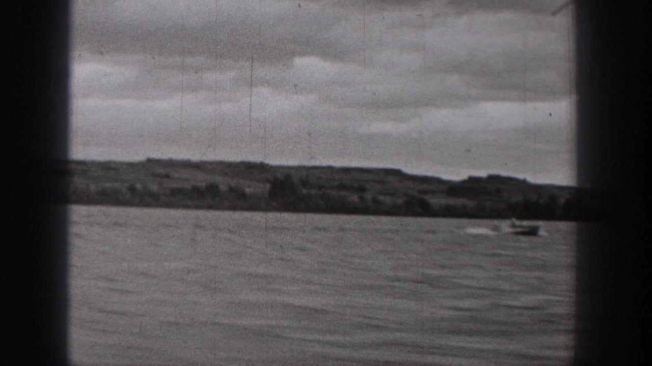 1938 Washington 8mm frame showing a small boat far out on calm water, with a low shoreline and overcast sky beyond dark film borders.