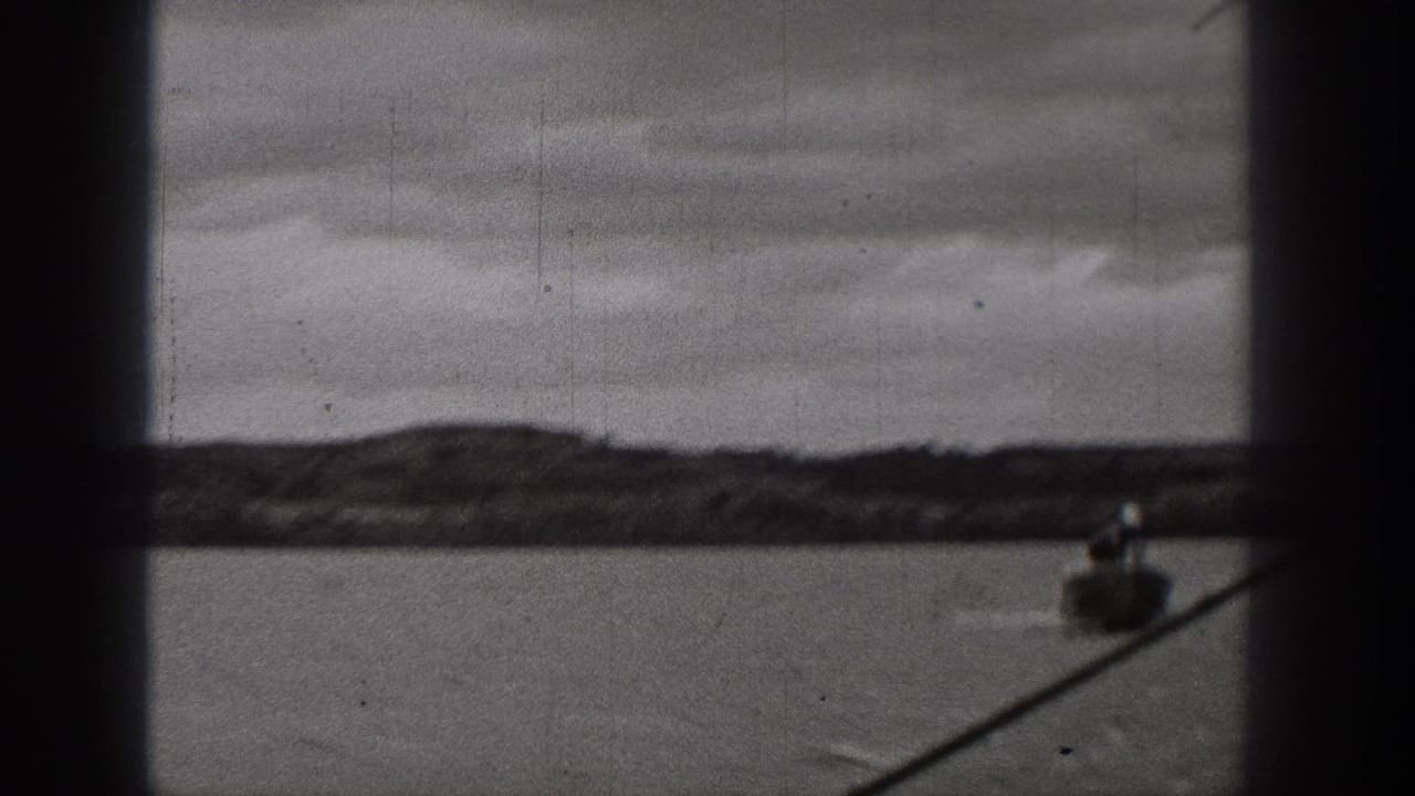 1938 Washington 8mm frame showing a small boat low in the composition, water, distant shore, overcast sky, and a diagonal dark foreground line.