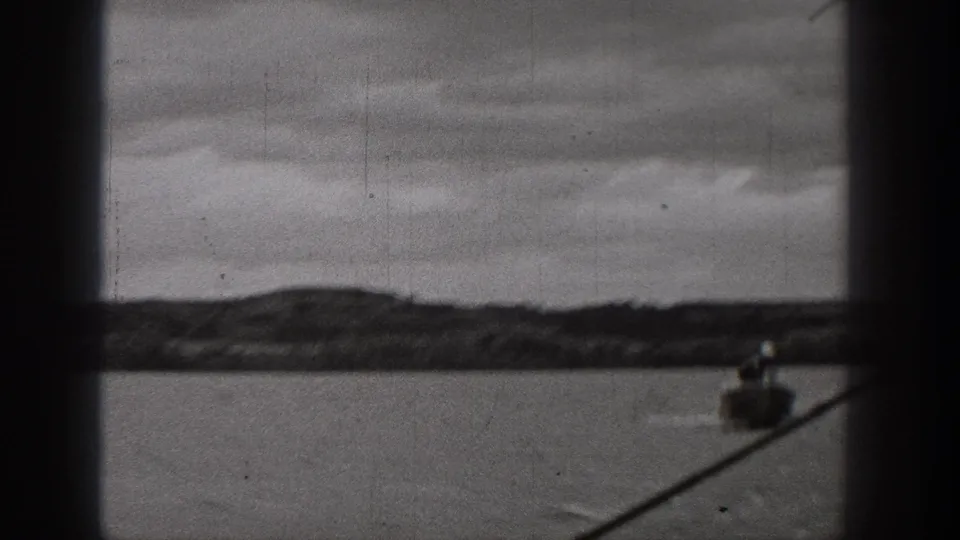 1938 Washington 8mm frame showing a small boat low in the composition, water, distant shore, overcast sky, and a diagonal dark foreground line.