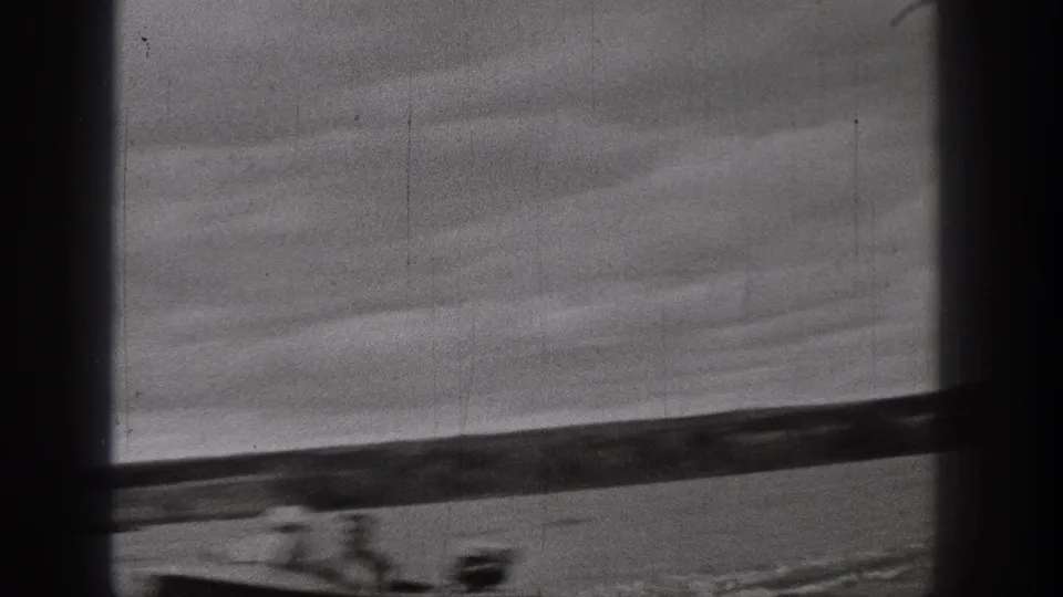 1938 Washington home-movie frame with calm water, low shoreline, heavy cloud cover, dark borders, and a faint boat wake near the bottom edge.
