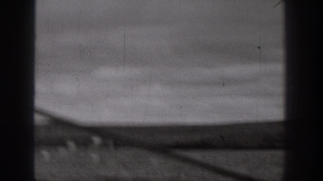 1938 Washington 8mm frame showing a blurred rural dirt road or plain through dark vertical bars, with hazy sky above.
