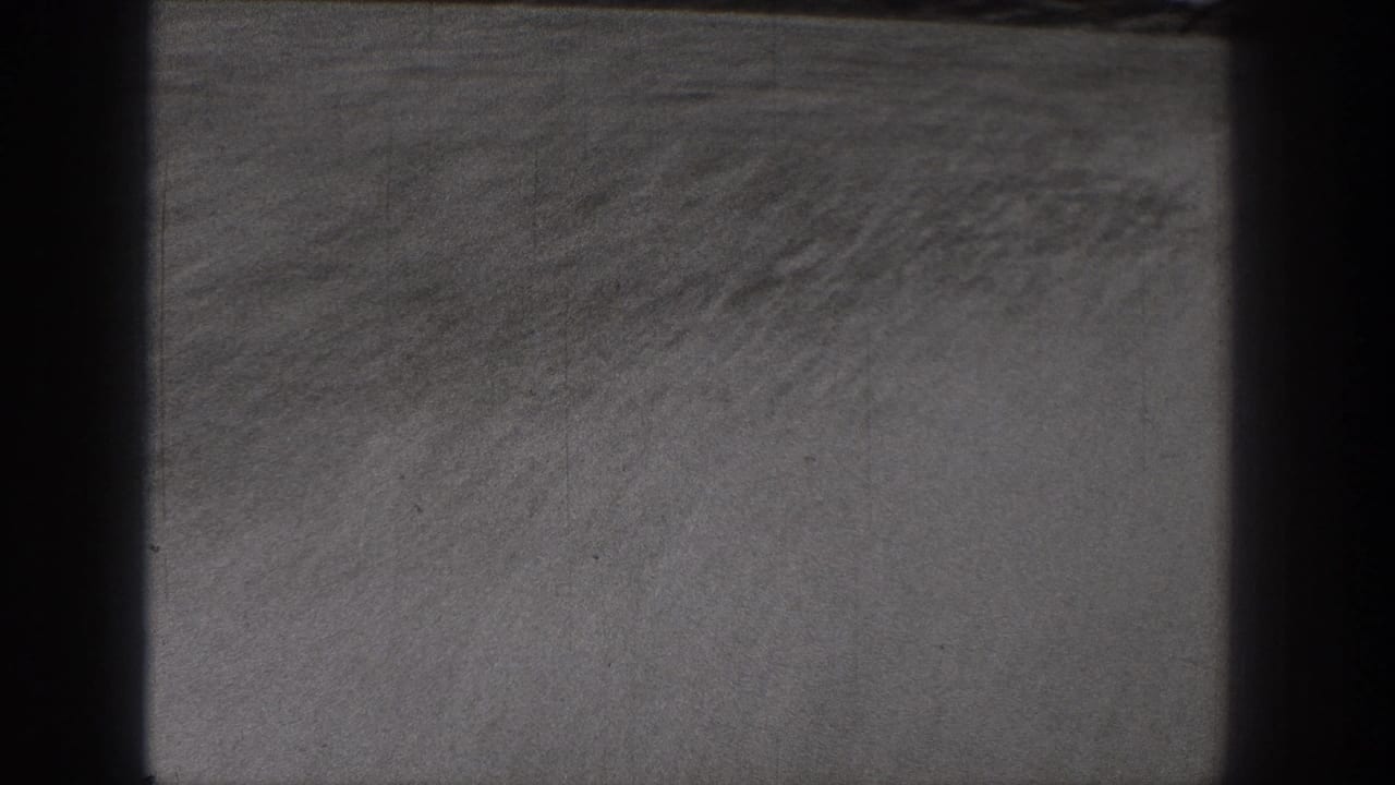 Monochrome 8mm view of dry open ground in Washington, with a faint horizon and dark framing at both sides.