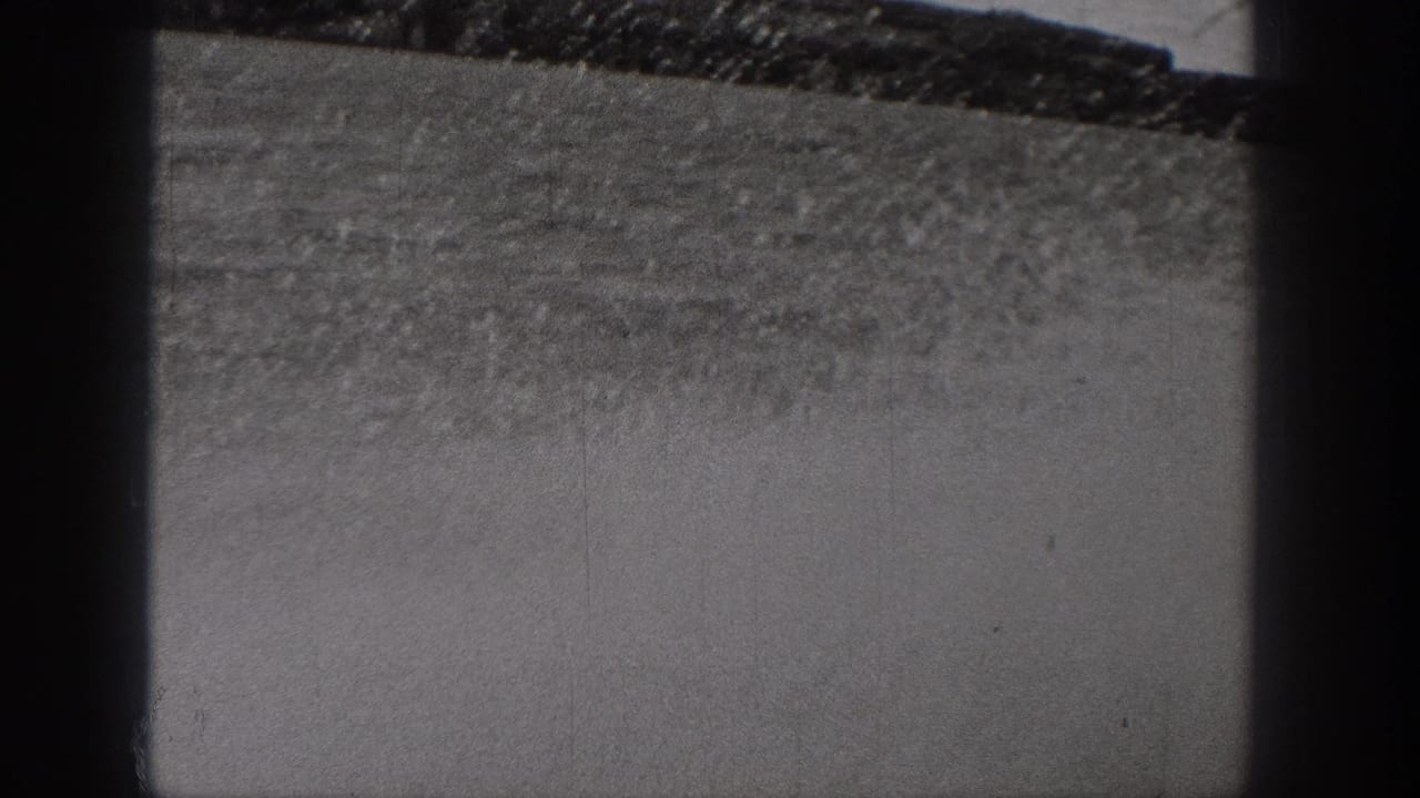 Monochrome 8mm frame from Washington showing rough dry ground and a sloping horizon, partly blocked by dark framing bars.