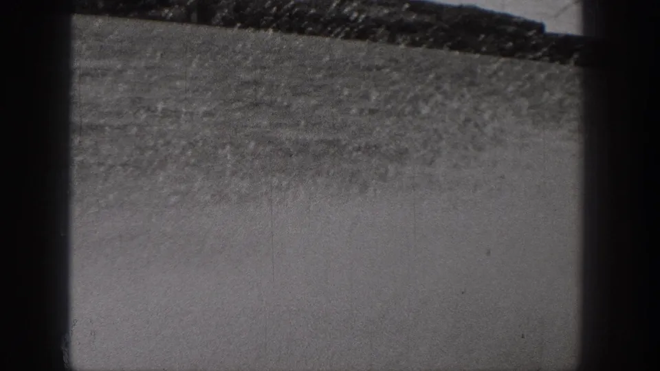 Monochrome 8mm frame from Washington showing rough dry ground and a sloping horizon, partly blocked by dark framing bars.