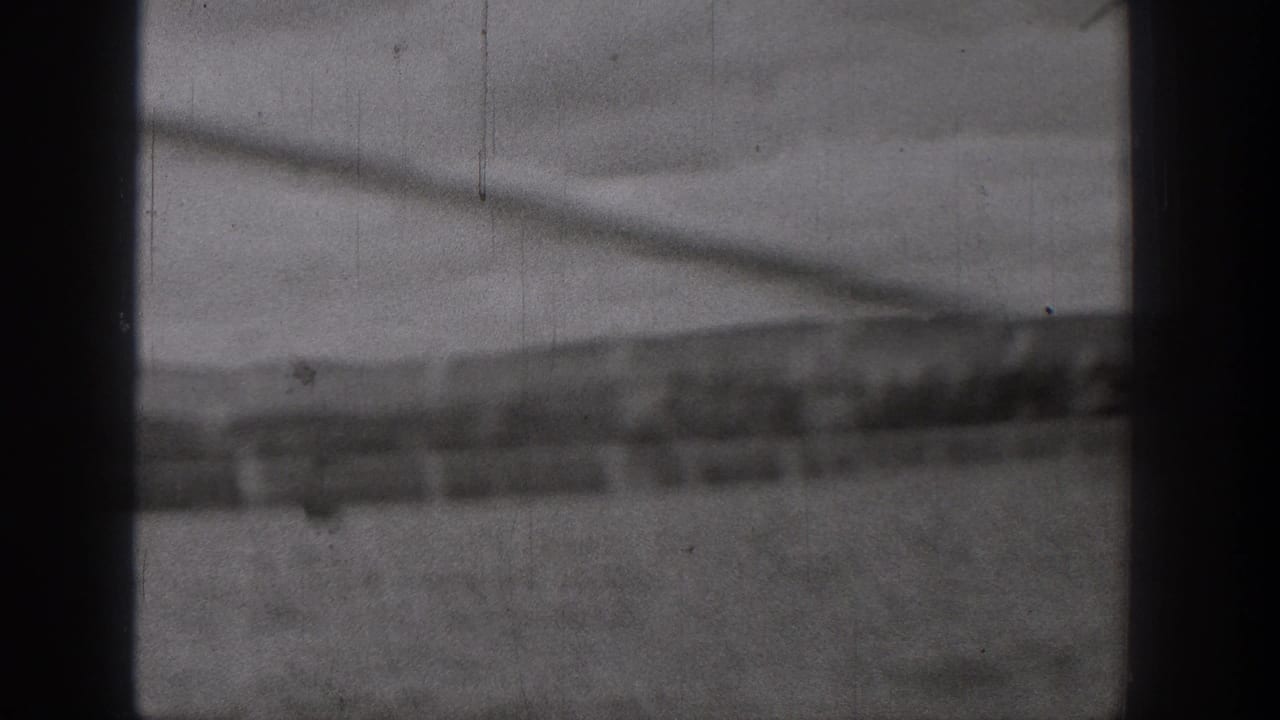 1938 Washington home-movie frame with blurred water, a darker shoreline strip, and visible film wear from a moving boat viewpoint.