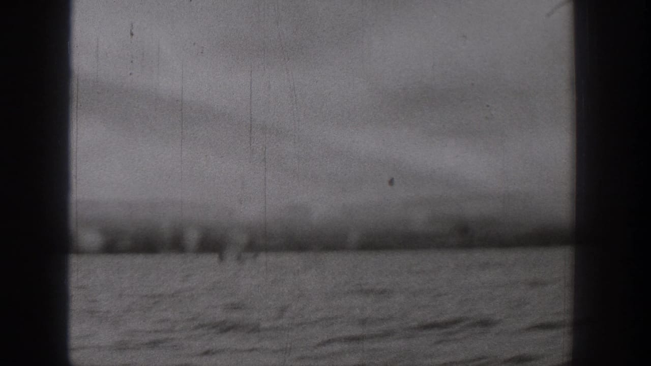 Black-and-white 8mm frame from the Washington cruise, showing water, a distant shore, cloudy sky, and a dark central frame edge.