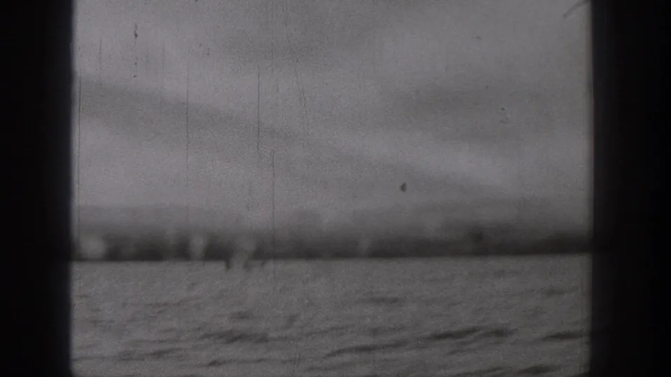 Black-and-white 8mm frame from the Washington cruise, showing water, a distant shore, cloudy sky, and a dark central frame edge.