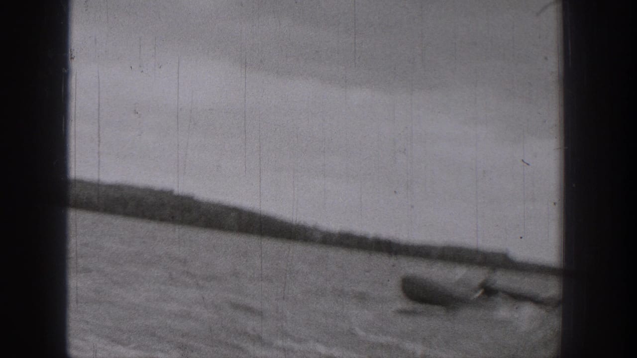 1938 Washington home-movie frame showing a small boat on rippled lake water, partly obscured by dark film or window framing.