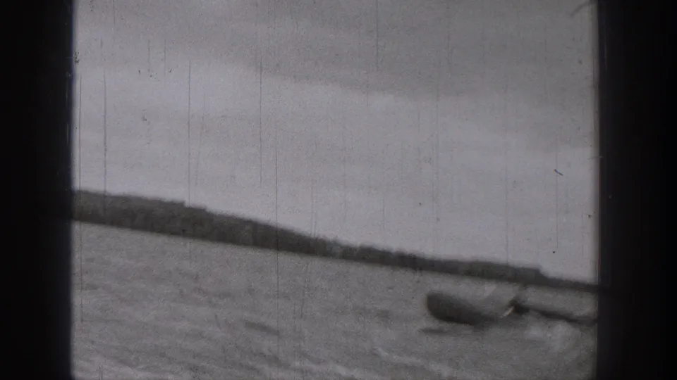 1938 Washington home-movie frame showing a small boat on rippled lake water, partly obscured by dark film or window framing.