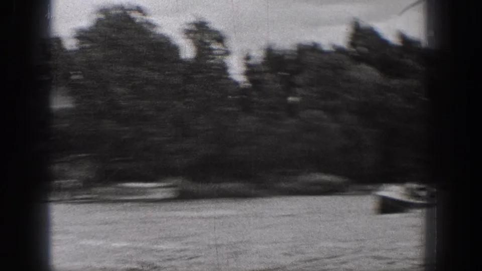 Motion-blurred 8mm view of lakeside trees and a small boat near the right edge, consistent with 1938 Washington home-movie footage.