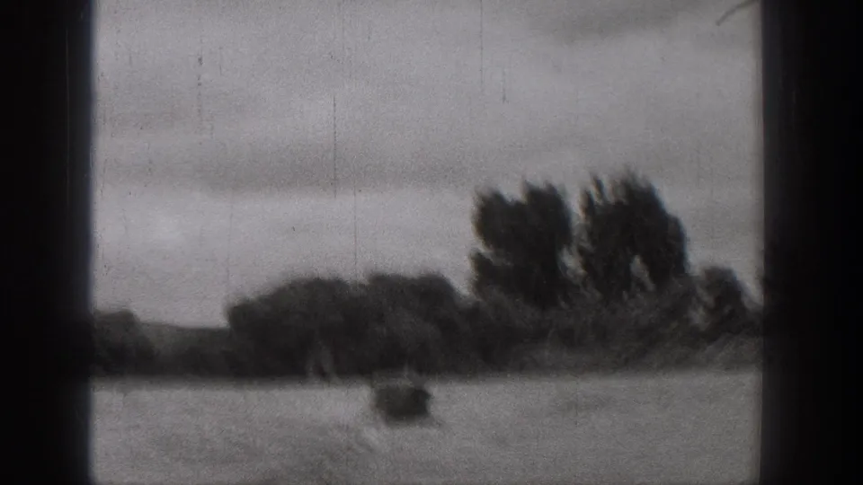 Black-and-white 8mm frame from Washington showing a small boat leaving a wake on a turbulent river under cloudy sky.