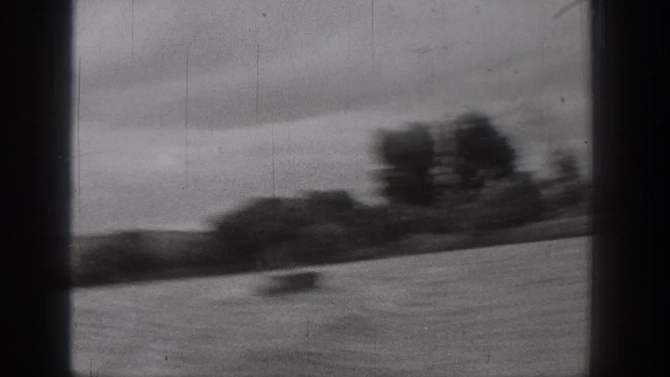 Washington 8mm home-movie frame showing a small blurred boat against a wide river and dark tree line under gray sky.