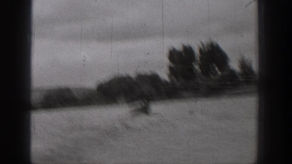 1938 Washington 8mm frame showing a dark-edged view over water toward trees and shoreline, with a boat blurred in motion near the left.