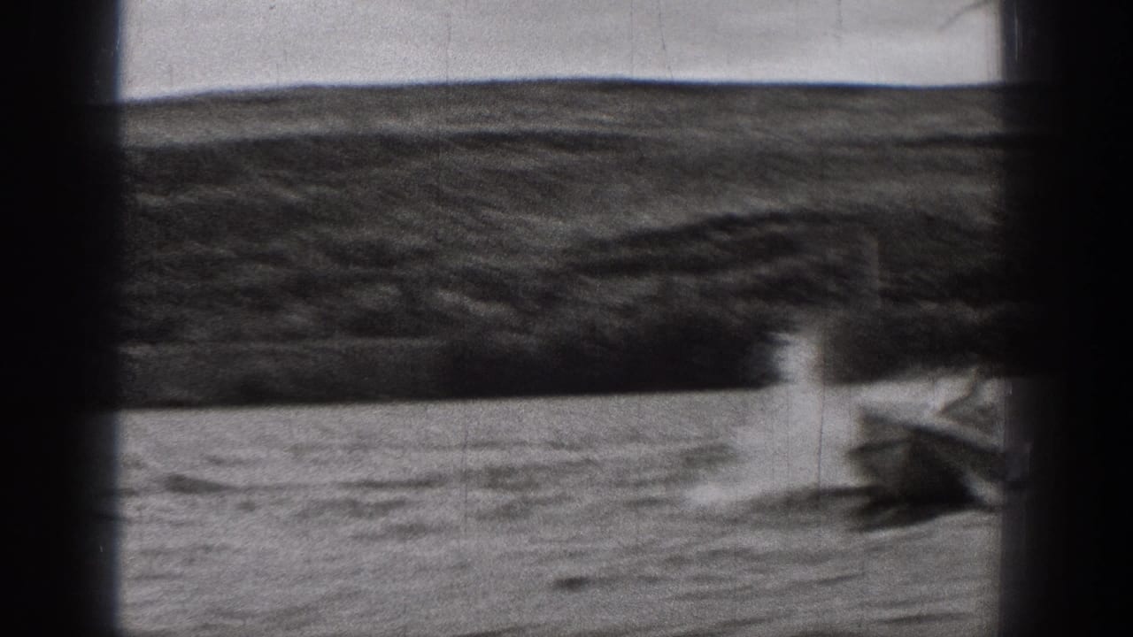 1938 Washington home-movie frame showing a speedboat producing spray and a foaming wake on rough water, with shoreline beyond.