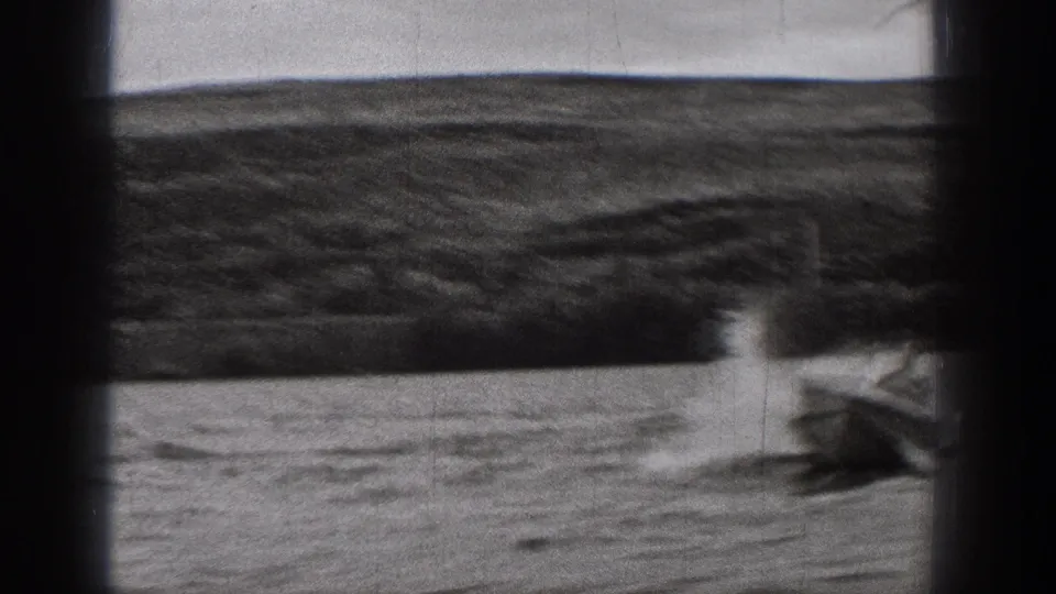1938 Washington home-movie frame showing a speedboat producing spray and a foaming wake on rough water, with shoreline beyond.