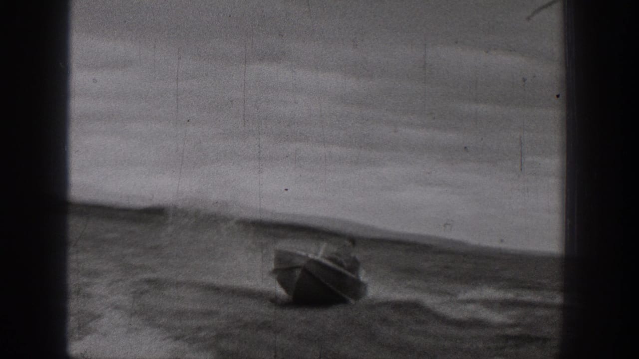 A small motorboat moves across choppy lake water in archival 1938 Washington home-movie footage, with hills faintly visible behind it.