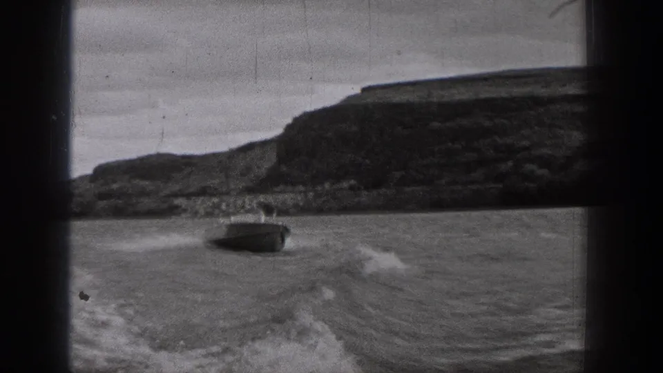 A motorboat travels ahead on a Washington lake, seen from a moving home-movie camera with wake lines and a dark hillside behind it.