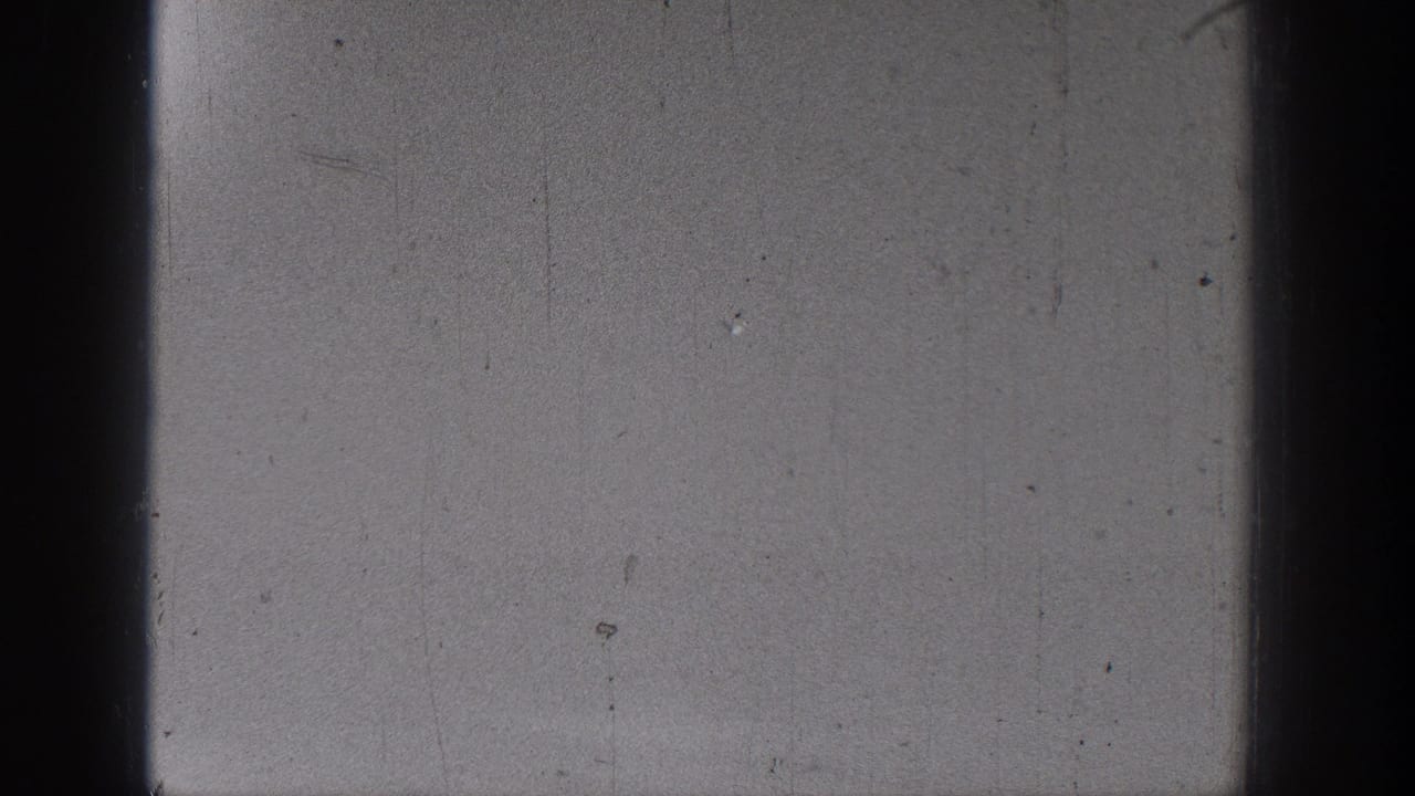 Dark-edged black-and-white film frame with grain, scratches, and no clearly visible subject.