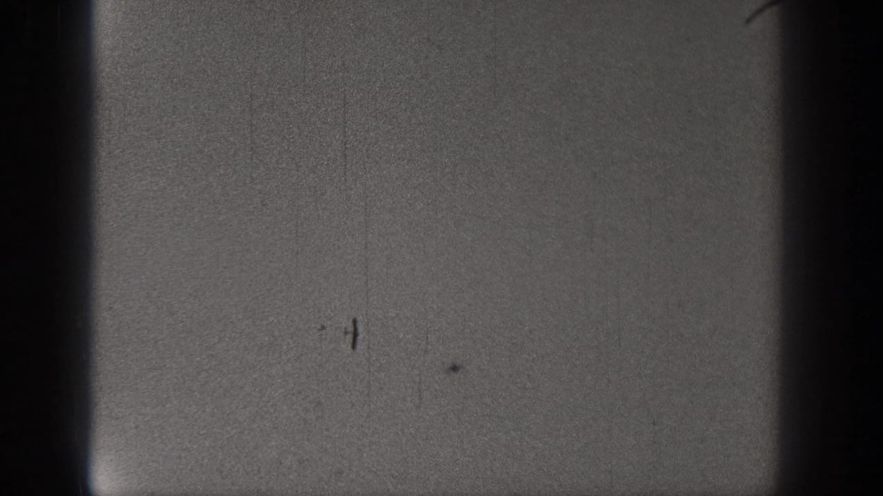 Dim black-and-white film frame with a central dark border and visible scratches.